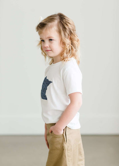 Toddler girl wearing a white minnesota logo on a white tee shirt. She is also wearing a long khaki skirt.