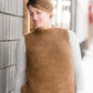 Woman wearing a tan colored fuzzy sweater vest. This vest has open sides and a ribbed bottom. It is also paired with a teal colored below the knee corduroy skirt.