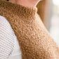 Woman wearing a tan colored fuzzy sweater vest. This vest has open sides and a ribbed bottom. It is also paired with a teal colored below the knee corduroy skirt.