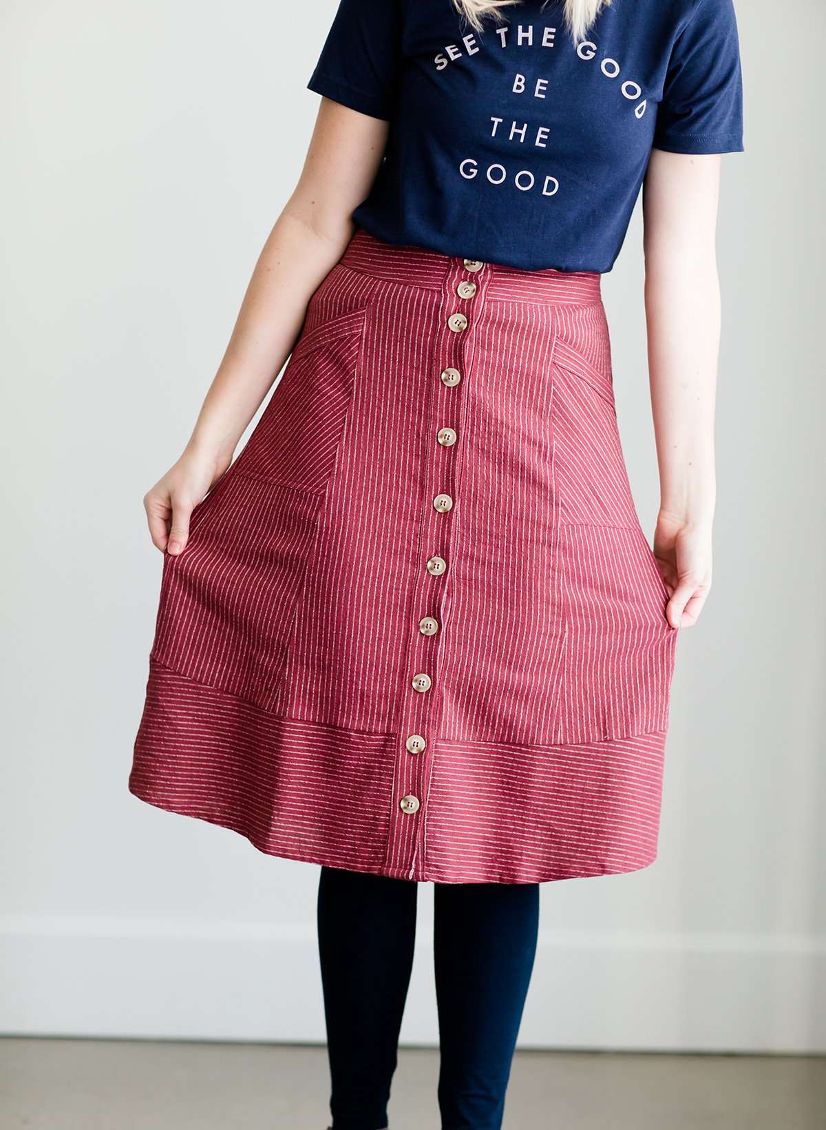 Woman wearing a modest below the knee striped skirt. This burgandy skirt has a button front, pockets, and A-line cut.