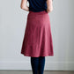 Woman wearing a modest below the knee striped skirt. This burgandy skirt has a button front, pockets, and A-line cut.