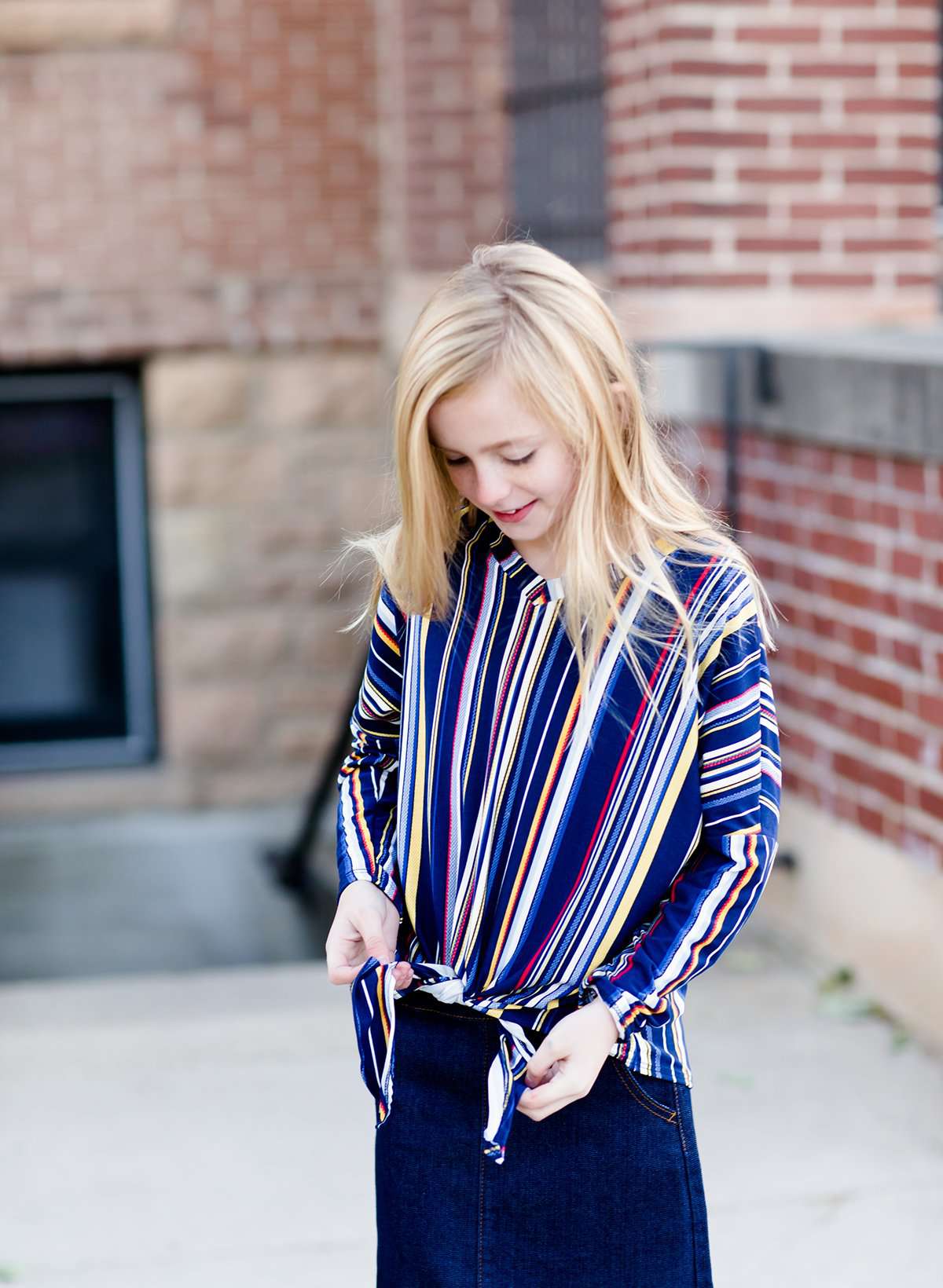 Young girl wearing a multi colored striped dolman top with a front tie. Colors in this top are navy, yellow, red, purple, green and white!