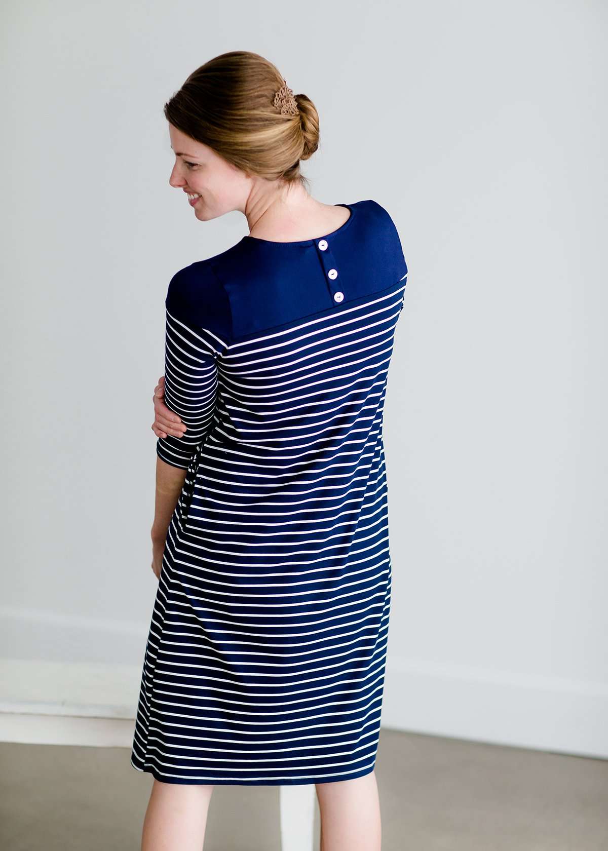 Woman wearing a striped navy and white midi dress with side pockets, long sleeves and back button details