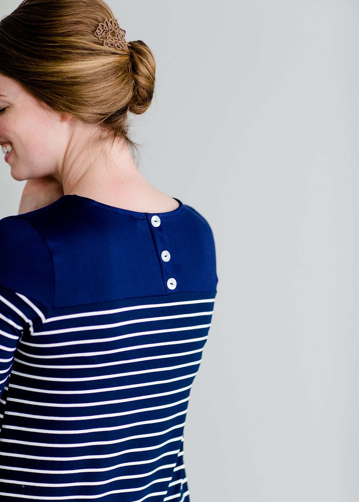 Woman wearing a striped navy and white midi dress with side pockets, long sleeves and back button details
