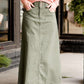 Woman wearing an olive, long modest cotton skirt. This skirt has no slit and is paired with a mauve sweater.