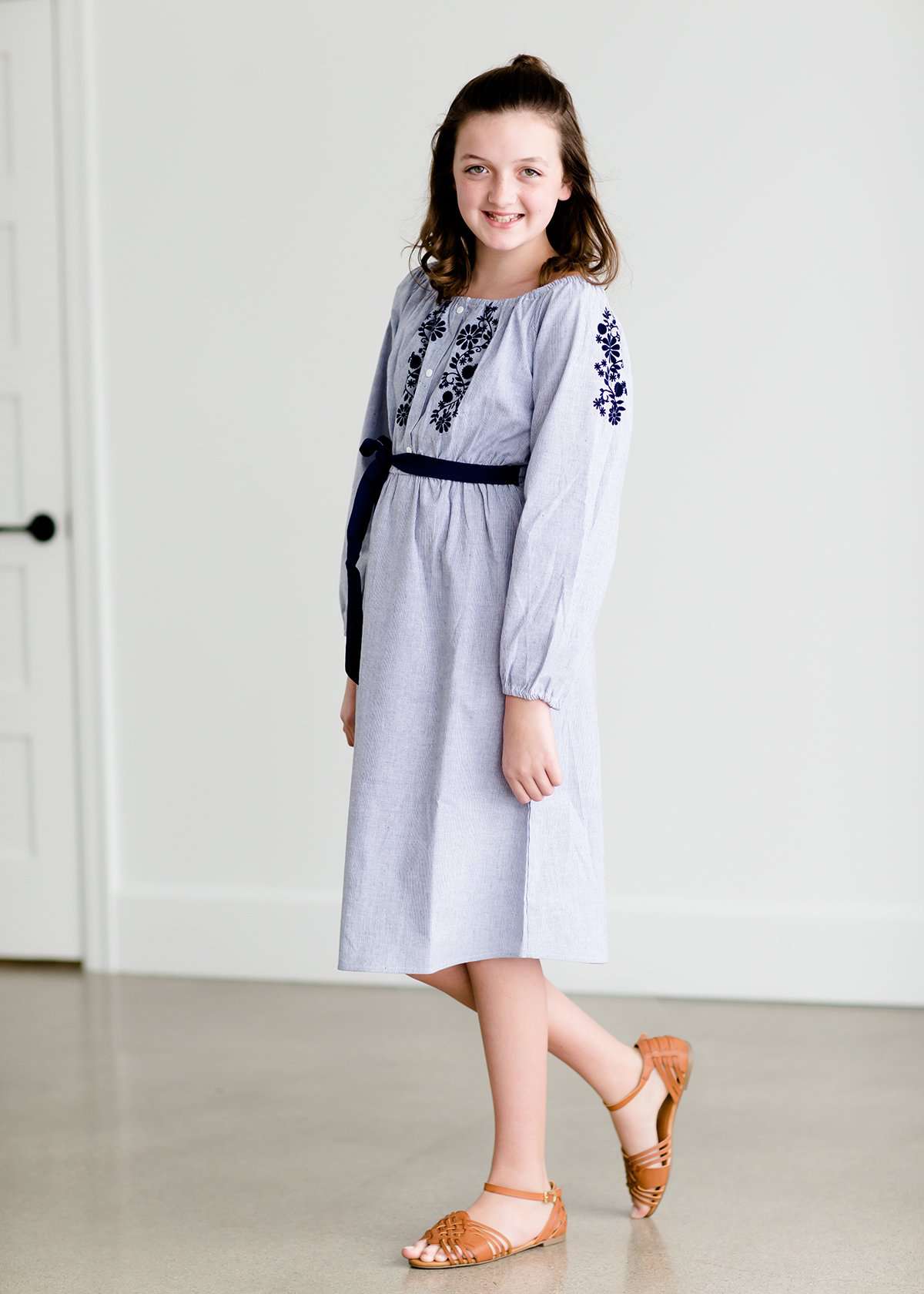 Tween wearing a navy boho pin stripe peasant dress with a self tie belt