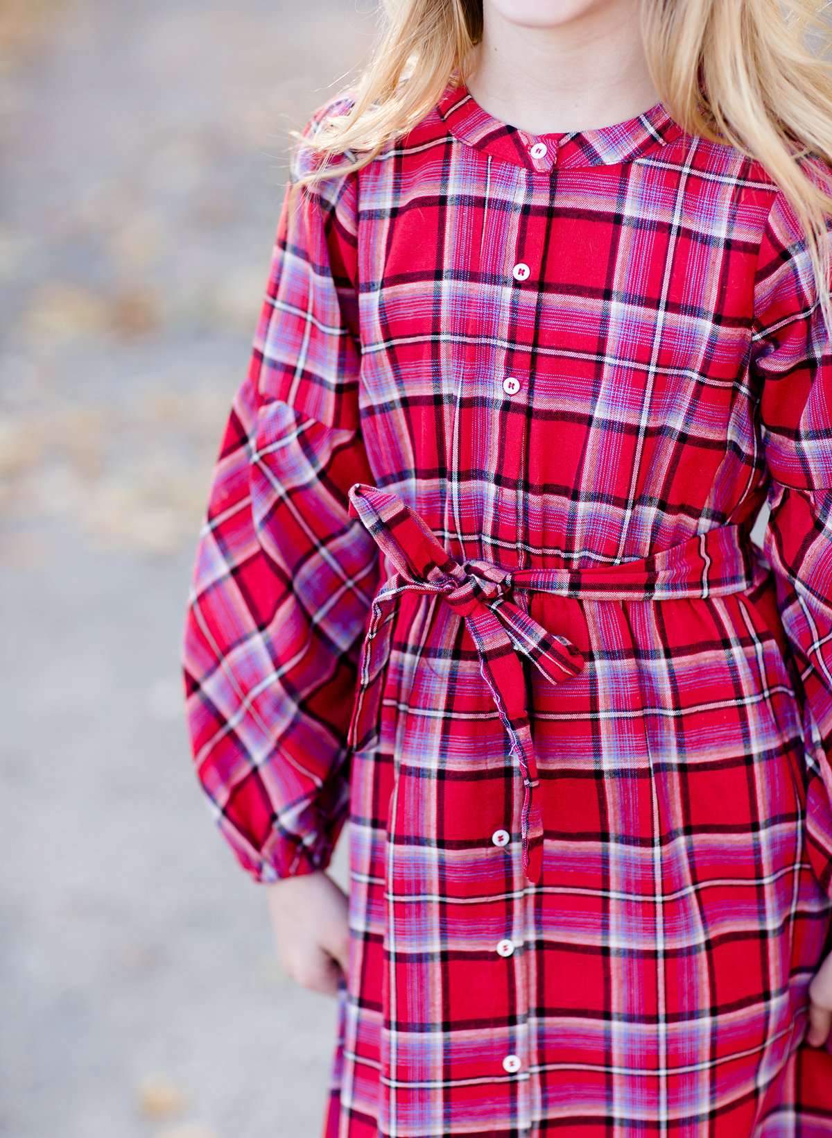 Young girl wearing a modest red plaid midi dress with balloon style sleeves. This dress also features a self tie fabric waist and is lined.