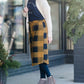 Woman wearing a modest plaid sweater style midi skirt. This skirt has an elastic waist and a tie front. It is paired with tights and short ankle boots.