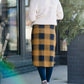 Woman wearing a modest plaid sweater style midi skirt. This skirt has an elastic waist and a tie front. It is paired with tights and short ankle boots.