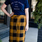 Woman wearing a modest plaid sweater style midi skirt. This skirt has an elastic waist and a tie front. It is paired with tights and short ankle boots.