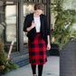 Woman wearing a modest plaid sweater style midi skirt. This skirt has an elastic waist and a tie front. It is paired with tights and short ankle boots.