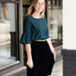 Woman wearing a black, velvet pleated midi skirt. This skirt has a gold accent around the elastic waistband. This modest skirt is paired with a teal, ruffle sleeve poets blouse.