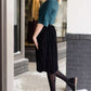 Woman wearing a black, velvet pleated midi skirt. This skirt has a gold accent around the elastic waistband. This modest skirt is paired with a teal, ruffle sleeve poets blouse.