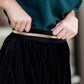 Woman wearing a black, velvet pleated midi skirt. This skirt has a gold accent around the elastic waistband. This modest skirt is paired with a teal, ruffle sleeve poets blouse.