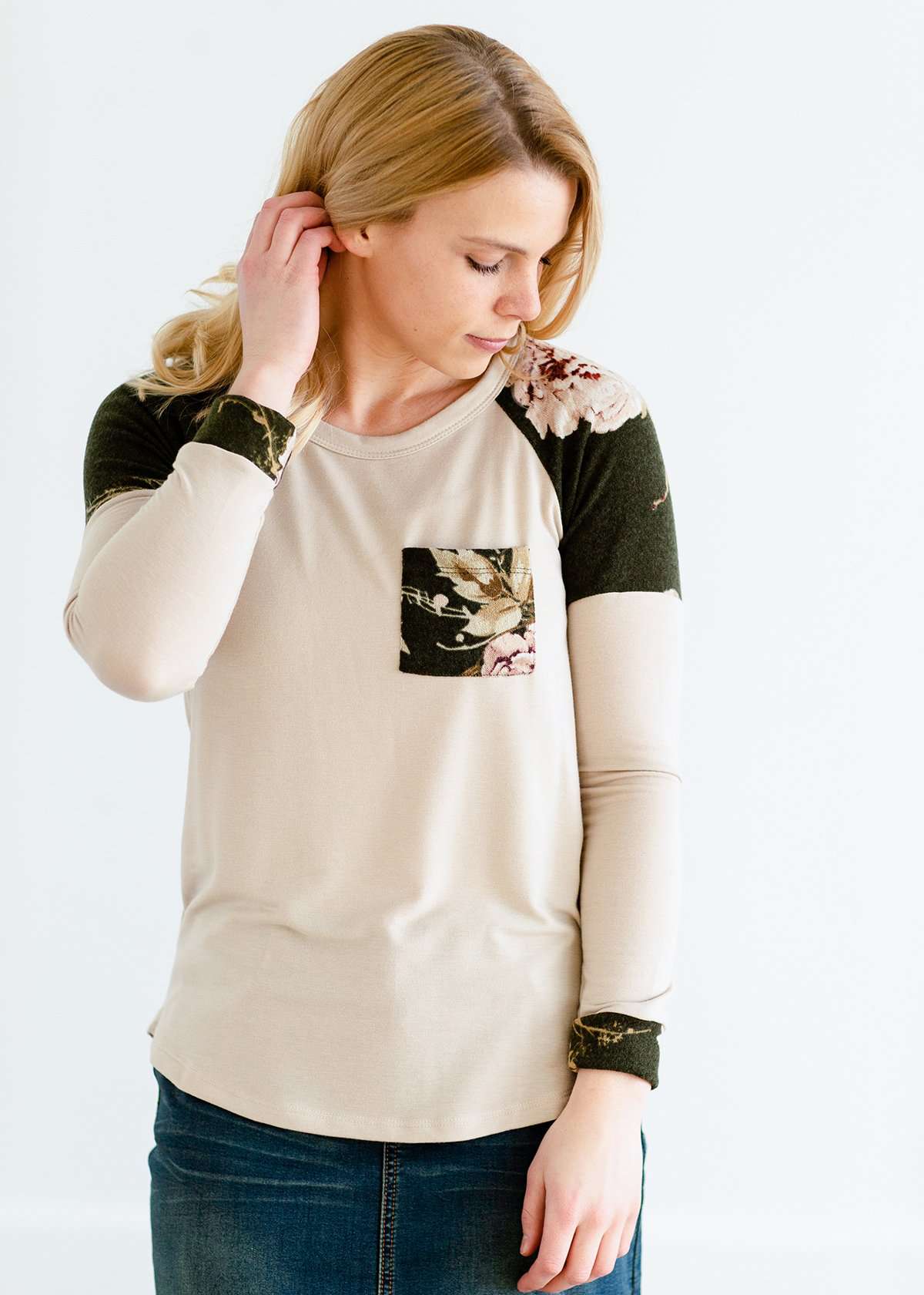 Woman wearing a taupe stretchy sweater with floral sleeves and pockets.