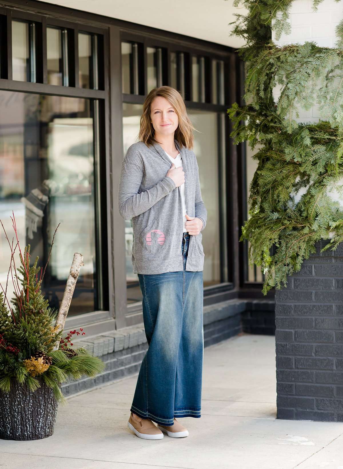 Woman standing in front of Inherit Clothing Company wearing a Minnesota screen printed, gray, open cardigan. The Minnesota screen print is pink.