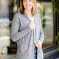 Woman standing in front of Inherit Clothing Company wearing a Minnesota screen printed, gray, open cardigan. The Minnesota screen print is pink.