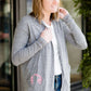 Woman standing in front of Inherit Clothing Company wearing a Minnesota screen printed, gray, open cardigan. The Minnesota screen print is pink.