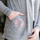 Woman standing in front of Inherit Clothing Company wearing a Minnesota screen printed, gray, open cardigan. The Minnesota screen print is pink.