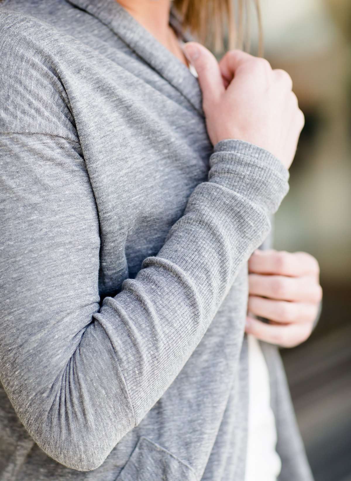 Woman standing in front of Inherit Clothing Company wearing a Minnesota screen printed, gray, open cardigan. The Minnesota screen print is pink.