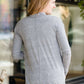 Woman standing in front of Inherit Clothing Company wearing a Minnesota screen printed, gray, open cardigan. The Minnesota screen print is pink.
