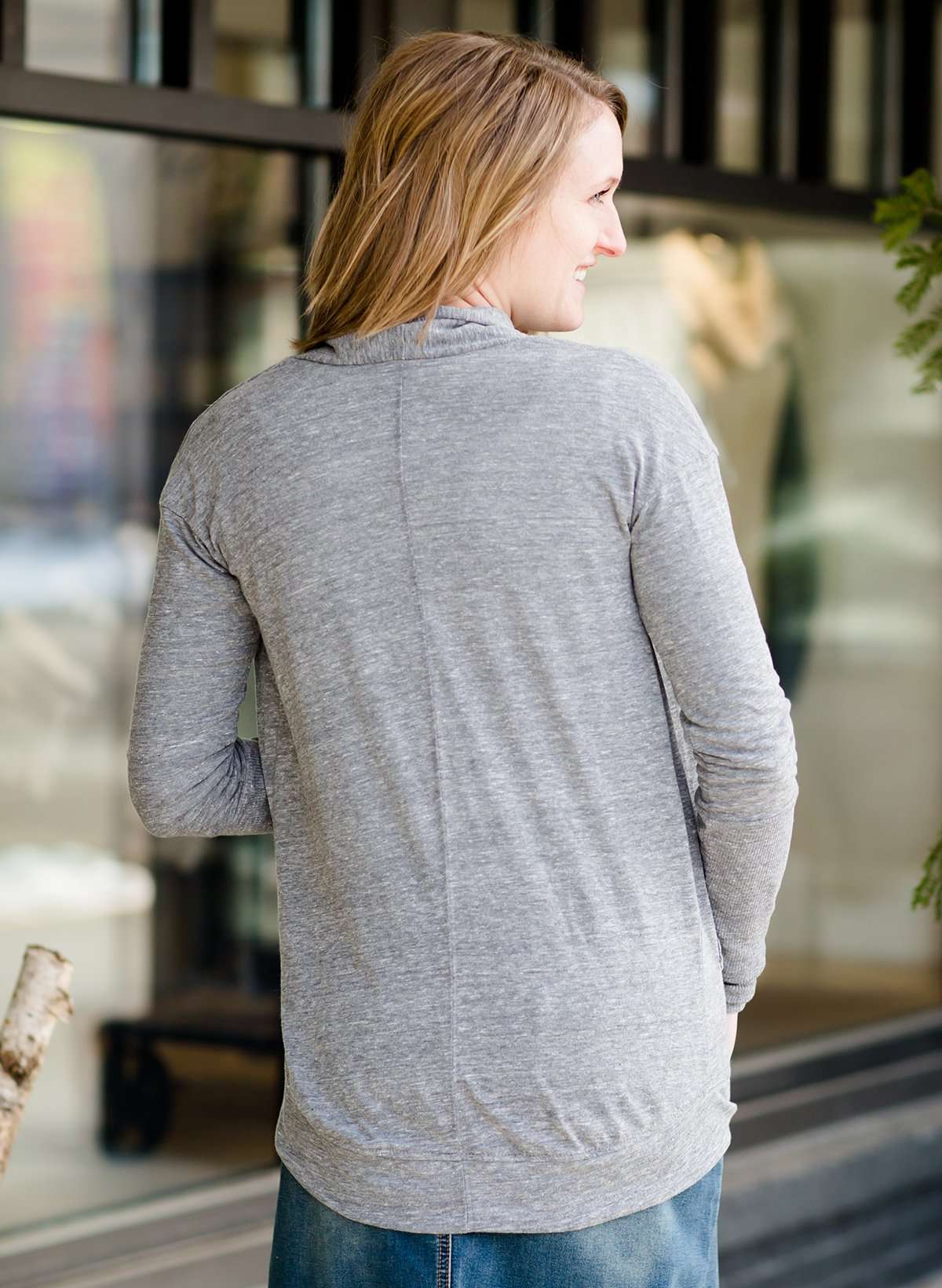 Woman standing in front of Inherit Clothing Company wearing a Minnesota screen printed, gray, open cardigan. The Minnesota screen print is pink.