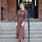 Woman on staircase wearing a rust colored, geometric print, smock maxi dress.