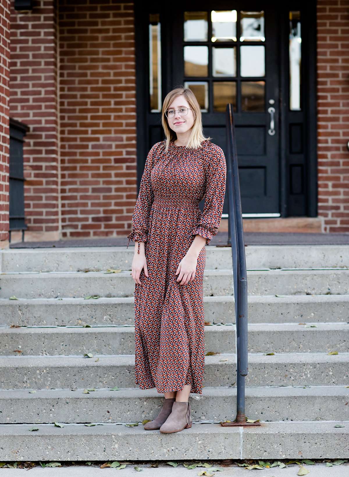 Woman on staircase wearing a rust colored, geometric print, smock maxi dress.