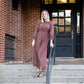 Woman on staircase wearing a rust colored, geometric print, smock maxi dress.