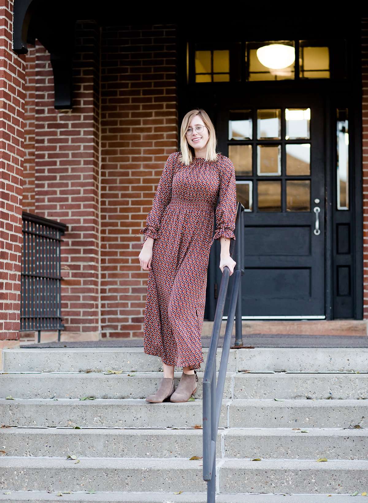 Woman on staircase wearing a rust colored, geometric print, smock maxi dress.