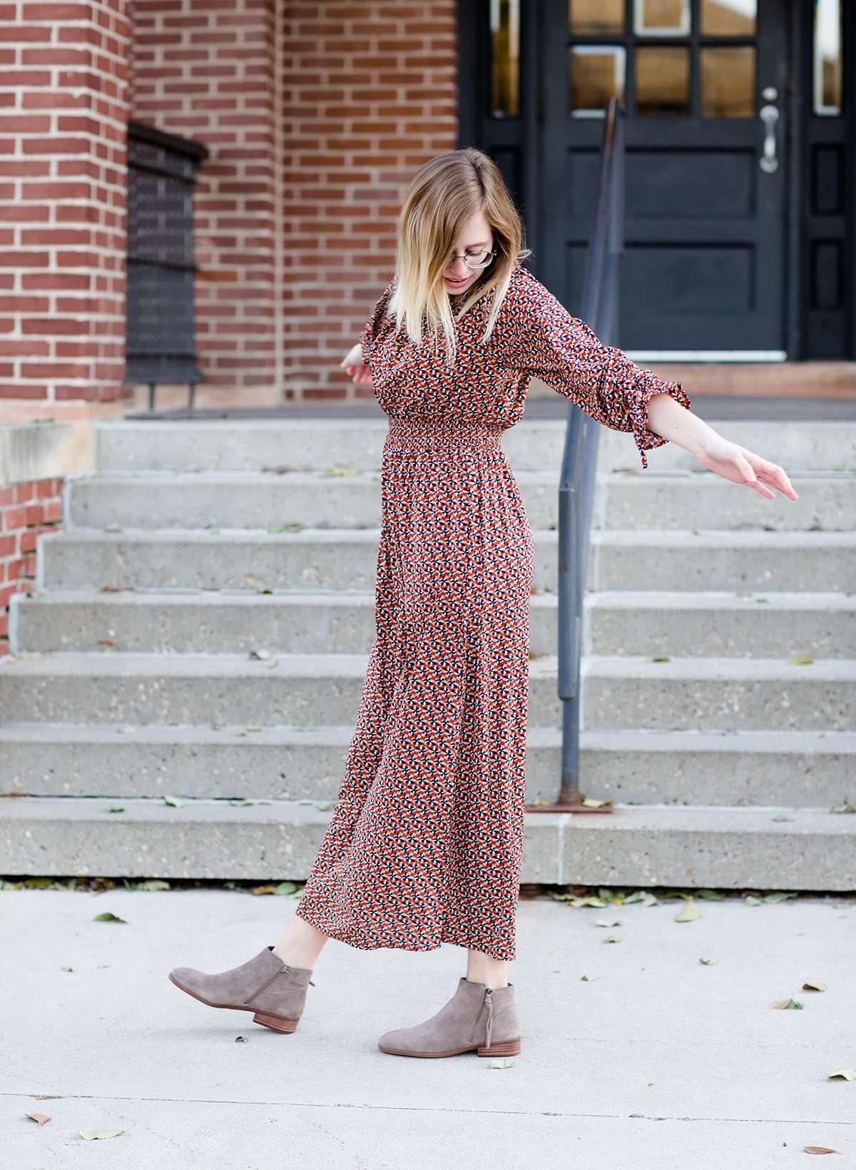 Woman on staircase wearing a rust colored, geometric print, smock maxi dress.