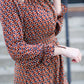 Woman on staircase wearing a rust colored, geometric print, smock maxi dress.