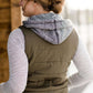 Woman wearing an anorak quilted vest with a zipper and hood. This vest comes in olive or black with gray accents.