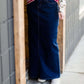 Woman wearing a long denim jean skirt that has a dark wash and a light wash. this is a long modest jean skirt.