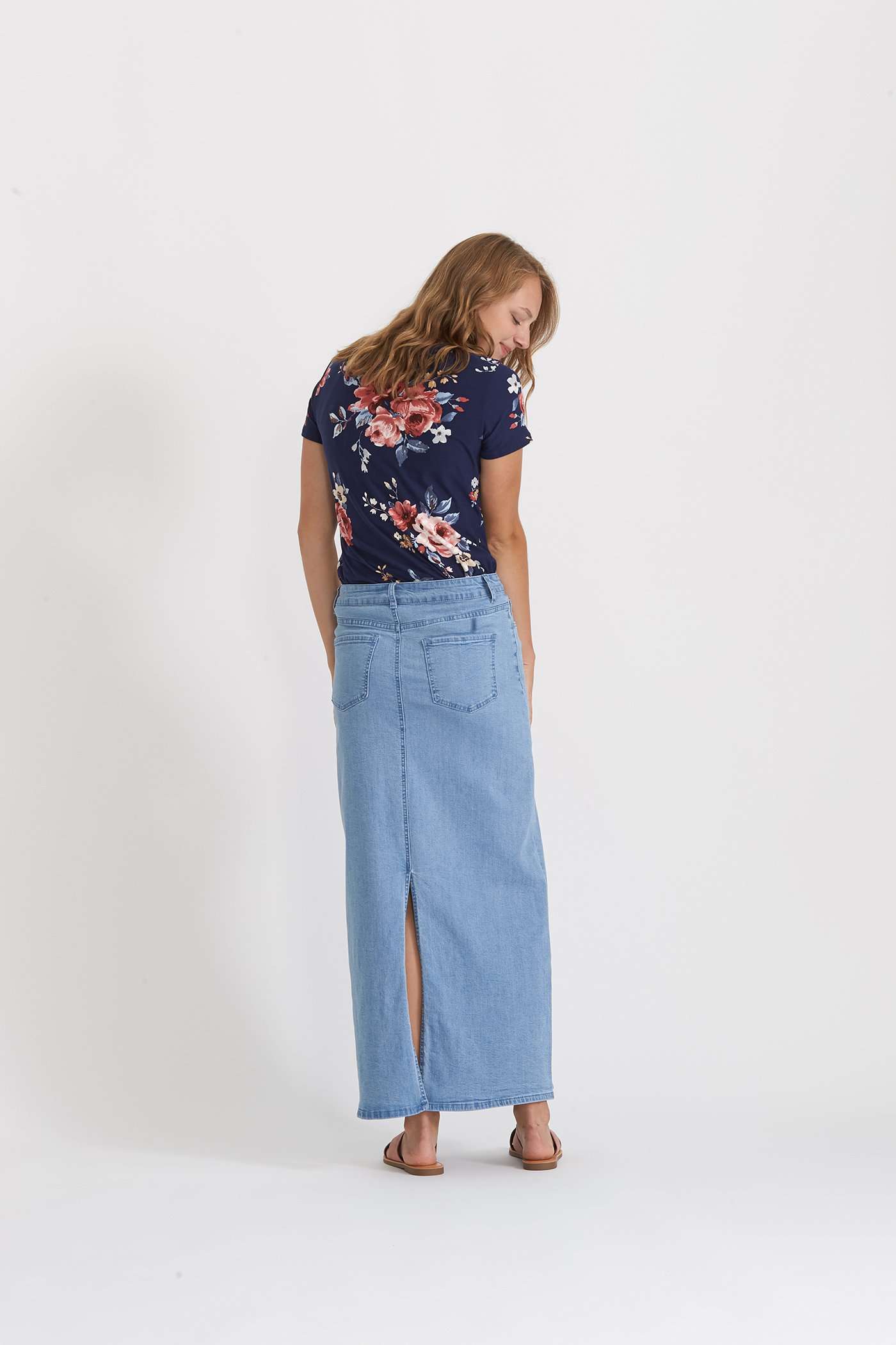 Woman wearing a long denim jean skirt that has a dark wash and a light wash. this is a long modest jean skirt.