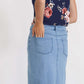 Woman wearing a long denim jean skirt that has a dark wash and a light wash. this is a long modest jean skirt.