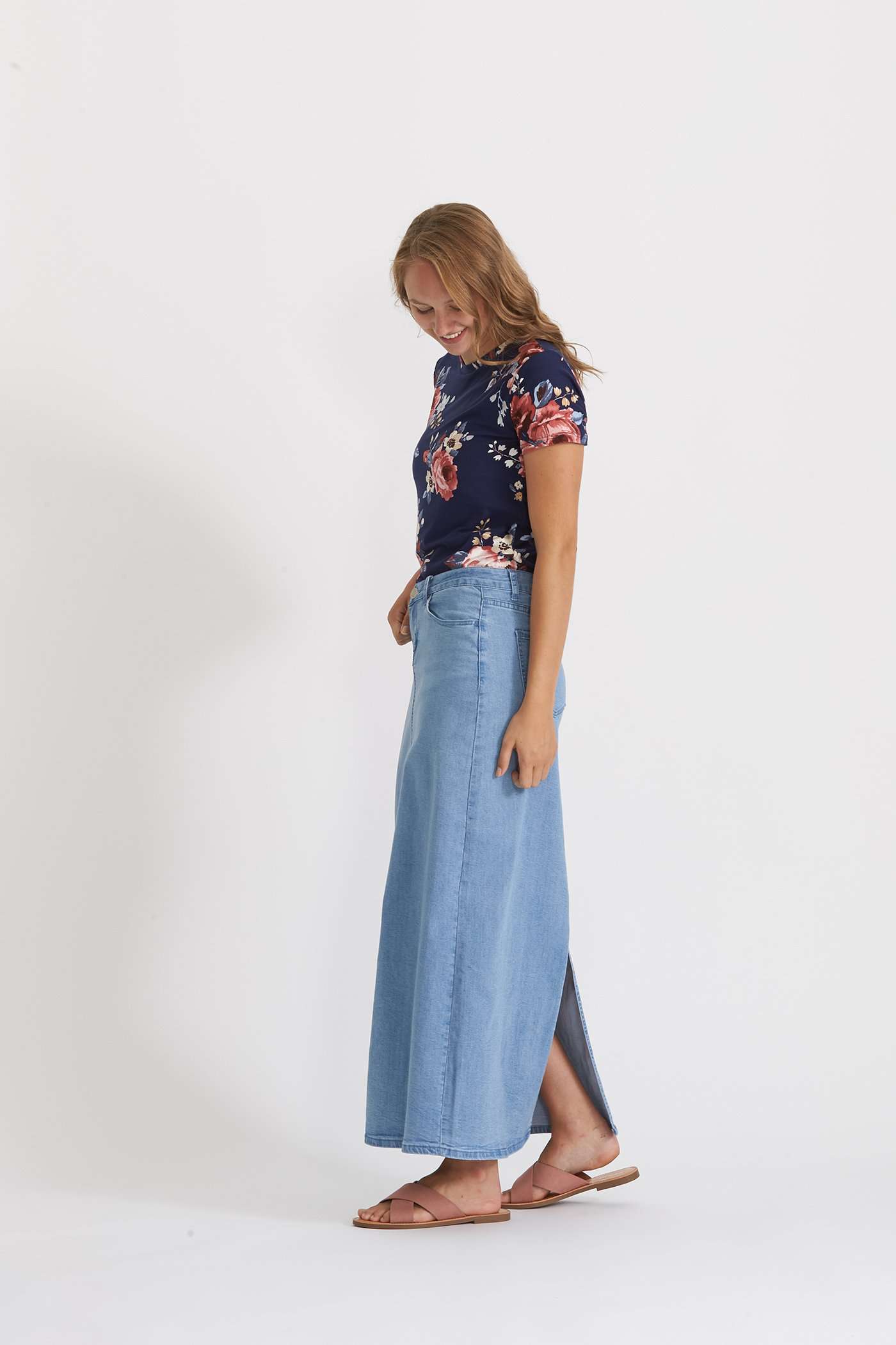 Woman wearing a long denim jean skirt that has a dark wash and a light wash. this is a long modest jean skirt.