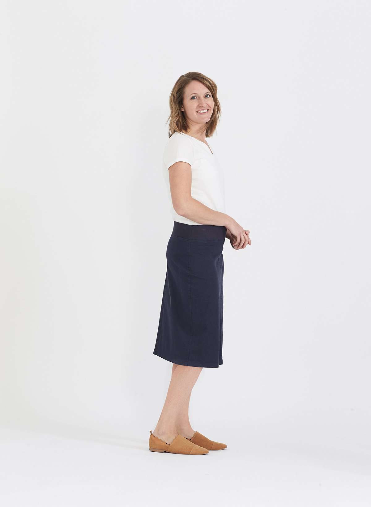 Woman wearing a colored, denim-like skirt with a elastic waistband. This is a modest skirt that falls below the knee. It comes in Burgundy, olive, khaki, black and navy. It is also paired with a white v-neck t-shirt.