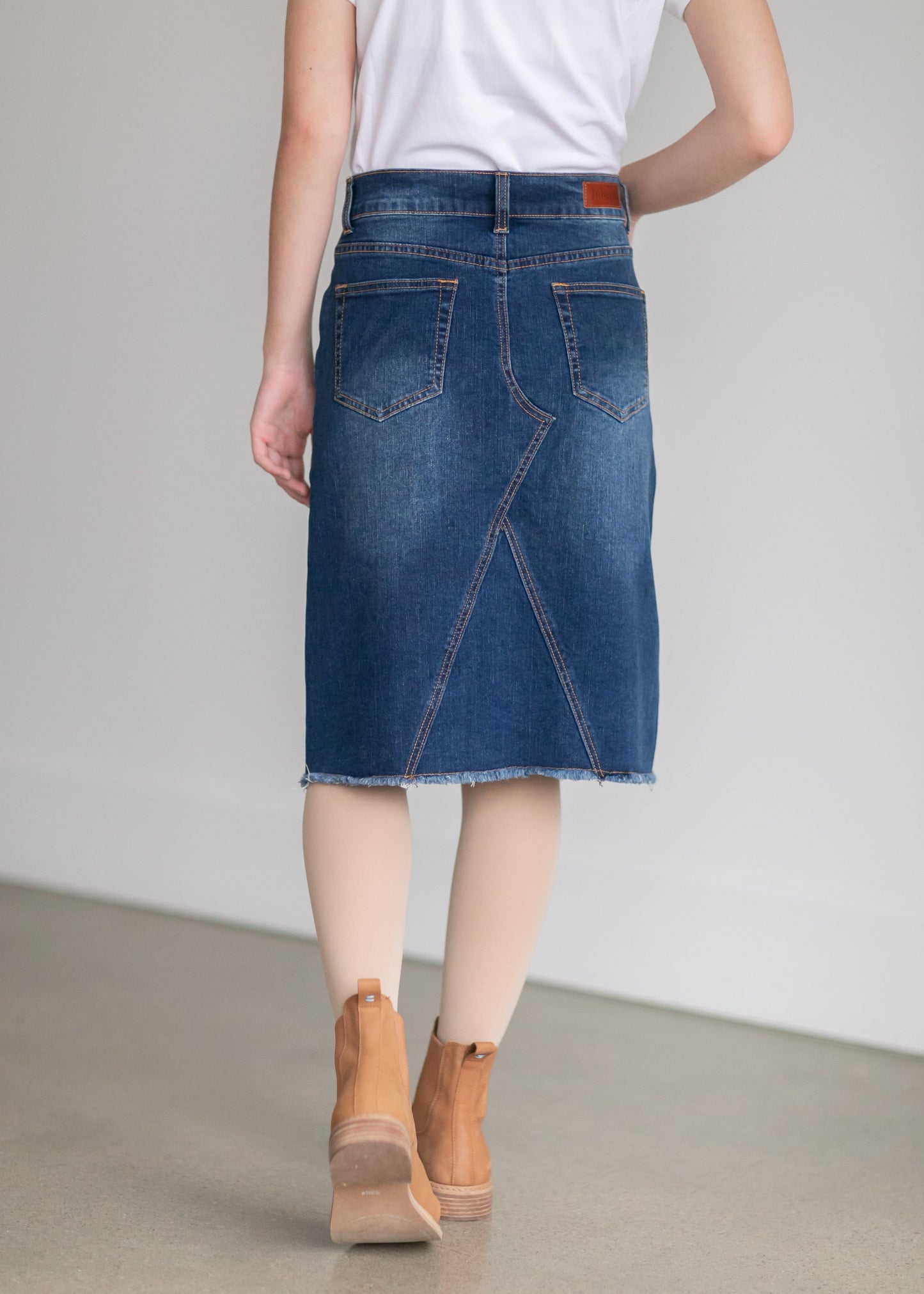 The Riley Frayed Hem Denim Midi Skirt is an Inherit Design that is full of lovely details! It is tailored in a slight a-line fit and super comfortable for anyone wanting that timeless look! This skirt is a darker wash with contrast stitching with a v-stitch in the front and back. You will love the raw bottom hem and the faux leather patch on the back!