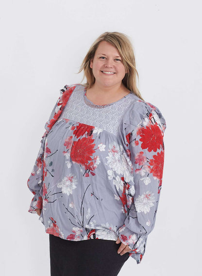 Plus size woman wearing a ruffle and floral gray blouse. This blouse has a key hole back and long sleeves. 