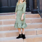 Young girl wearing a sage colored ruffle dress with lace trim on the tiers of the ruffles.