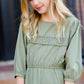 Young girl wearing a sage colored ruffle dress with lace trim on the tiers of the ruffles.