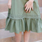 Young girl wearing a sage colored ruffle dress with lace trim on the tiers of the ruffles.