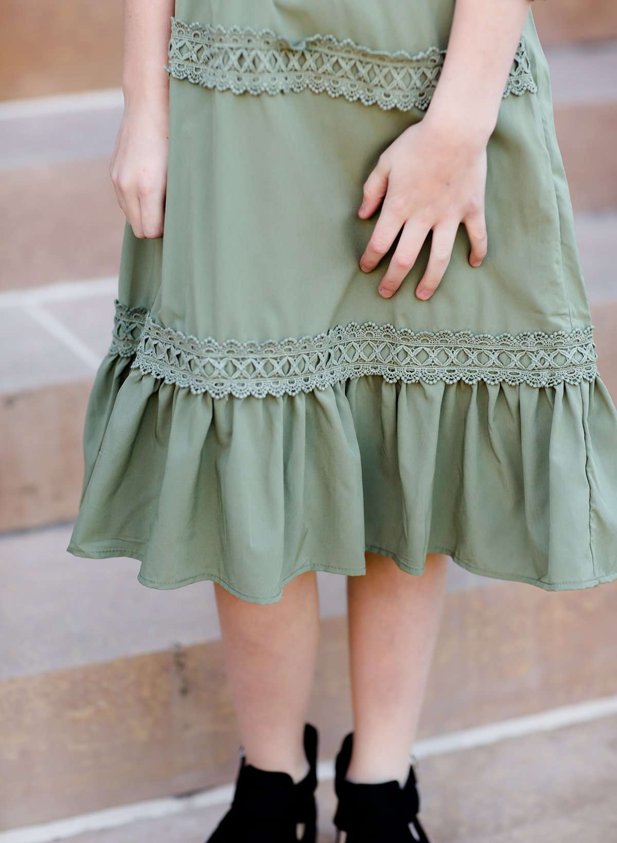 Young girl wearing a sage colored ruffle dress with lace trim on the tiers of the ruffles.