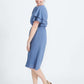 woman wearing a dusty blue empire waist dress with double ruffle sleeves that is lined and falls below the knee