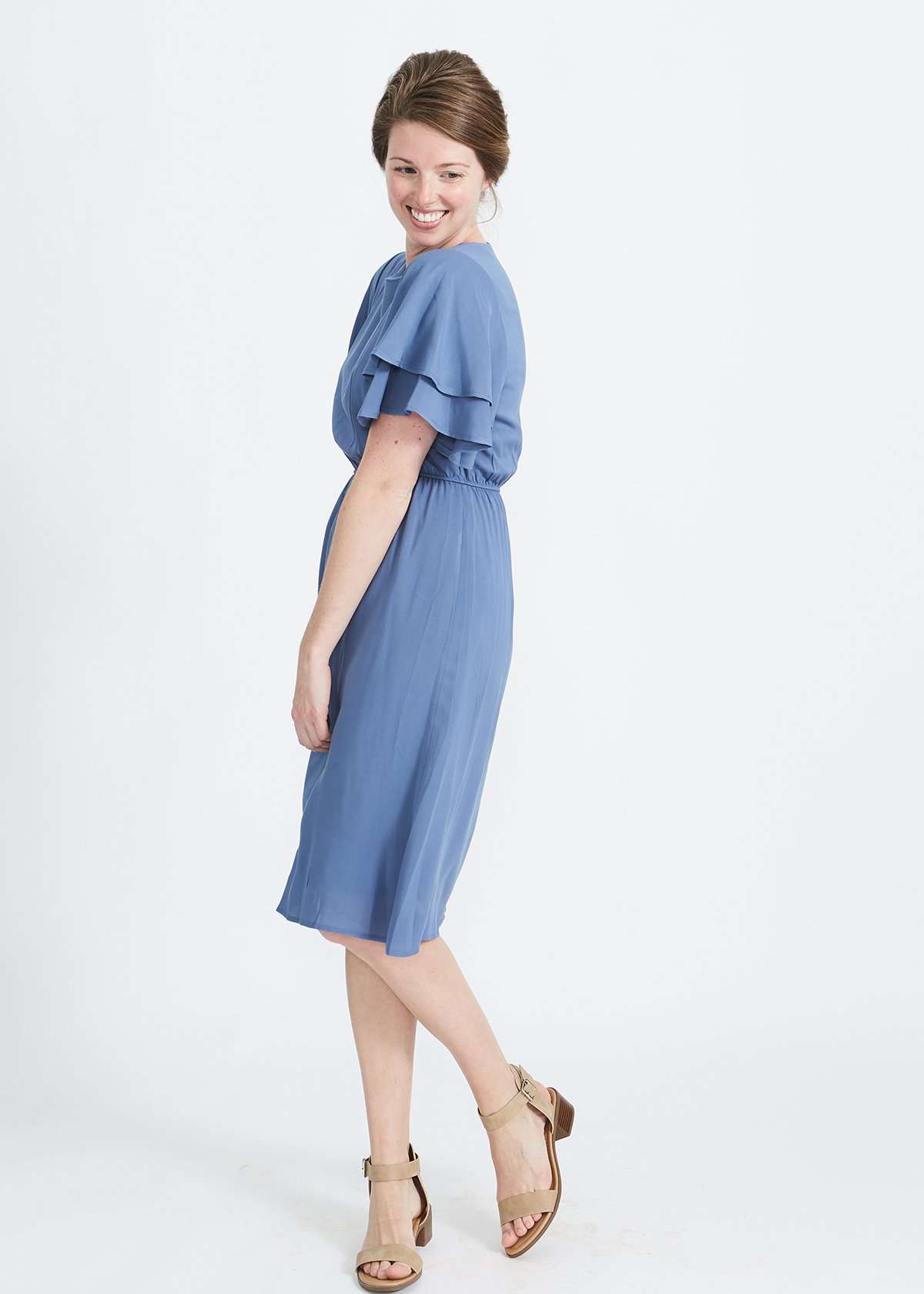 woman wearing a dusty blue empire waist dress with double ruffle sleeves that is lined and falls below the knee