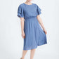 woman wearing a dusty blue empire waist dress with double ruffle sleeves that is lined and falls below the knee