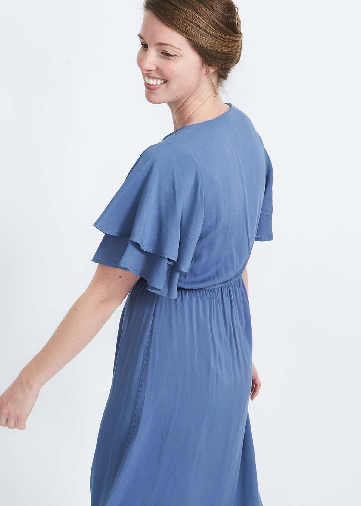 woman wearing a dusty blue empire waist dress with double ruffle sleeves that is lined and falls below the knee