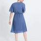 woman wearing a dusty blue empire waist dress with double ruffle sleeves that is lined and falls below the knee