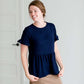 Woman wearing a navy peplum baby doll top that has ruffle details on the sleeves.